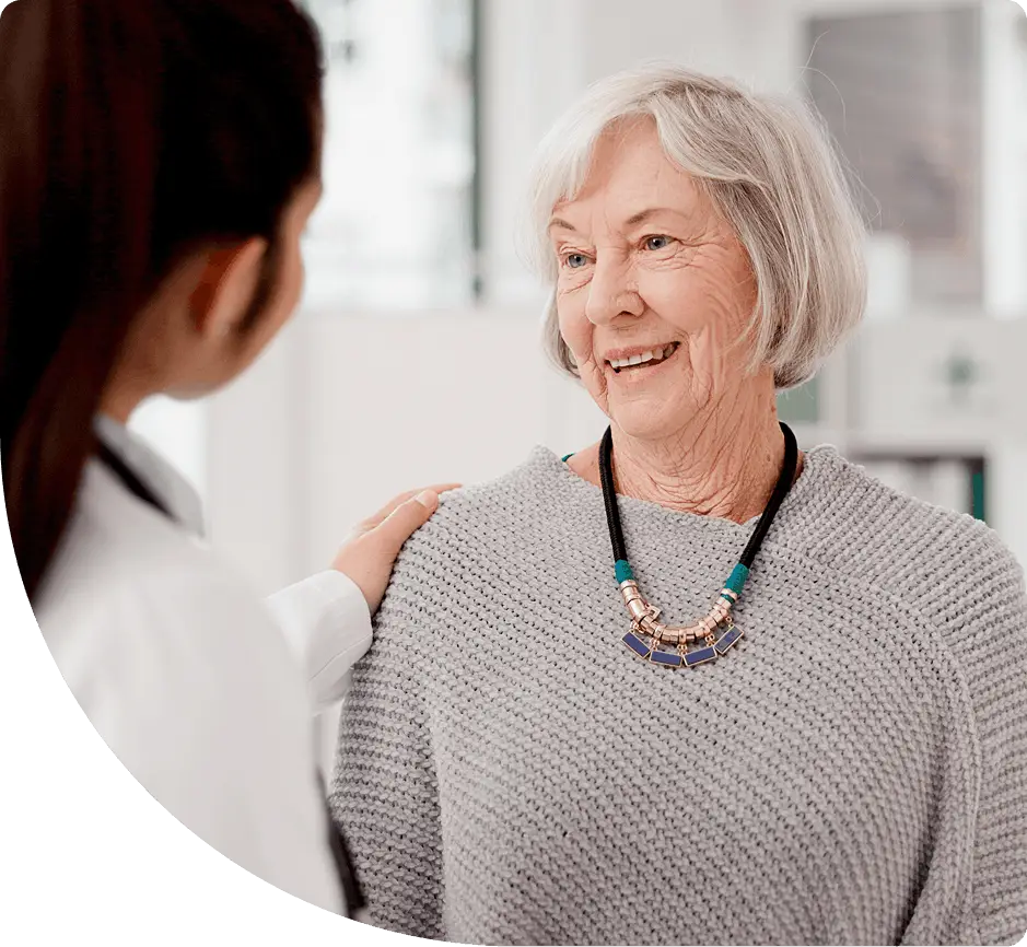A female healthcare provider with her back to the camera talks with an older female patient.